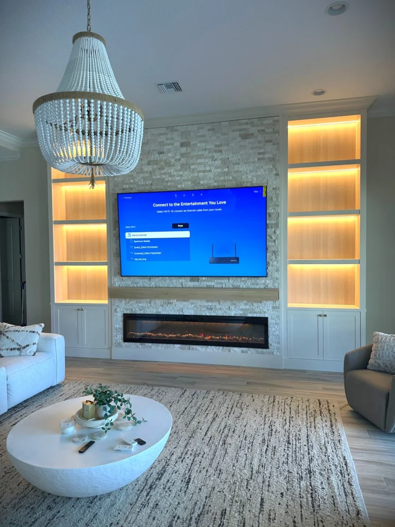 Completed stone fireplace media wall matching the project elevation Full completed light stone fireplace media wall with television, wood mantel, eight illuminated niches and base cabinets