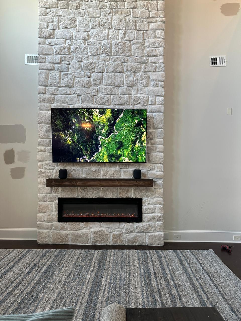 Front view of a completed custom limestone fireplace wall with TV, wood mantel and linear fireplace