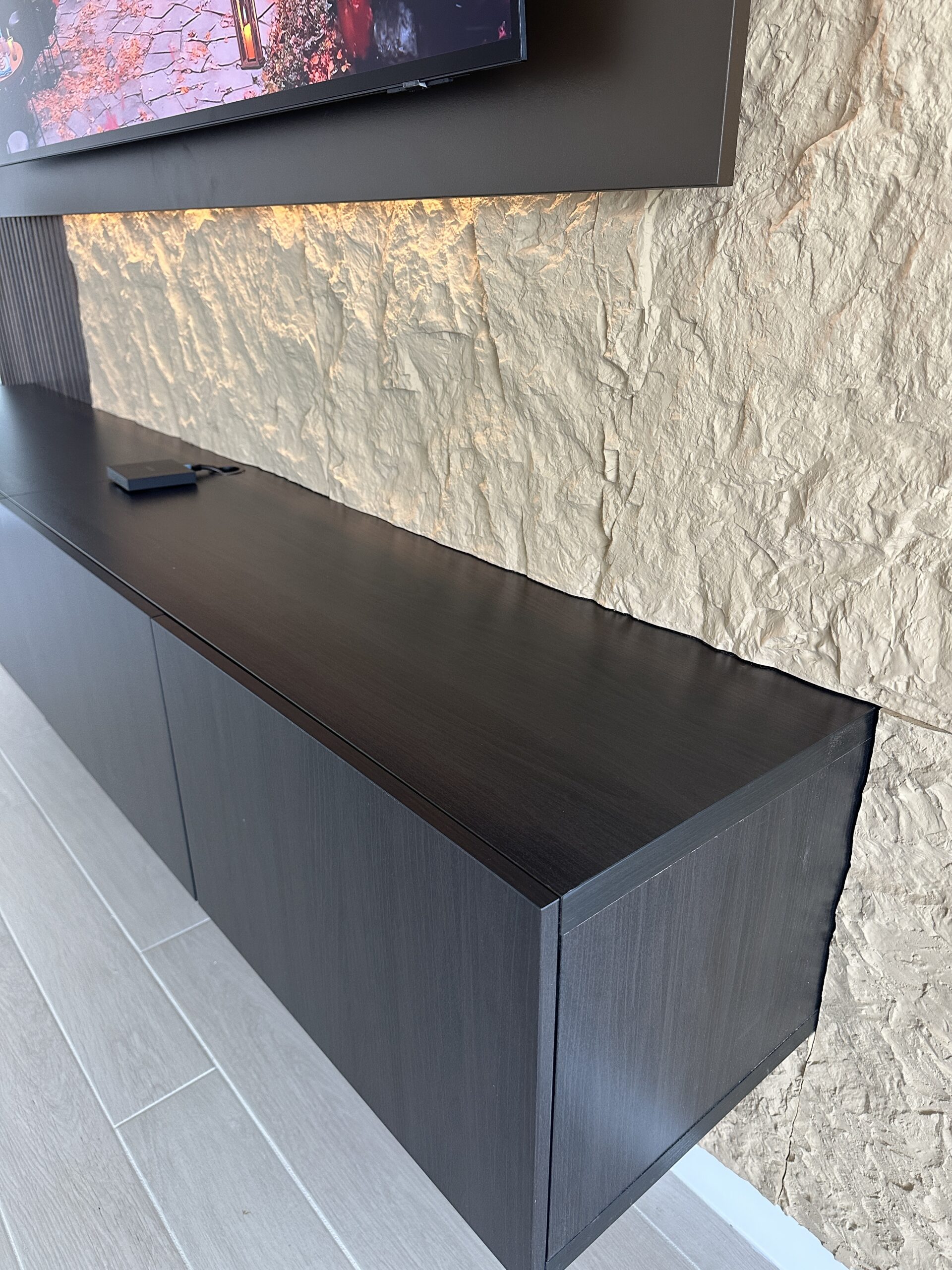 Detail of the dark floating media cabinet top, end panel and light textured wall finish