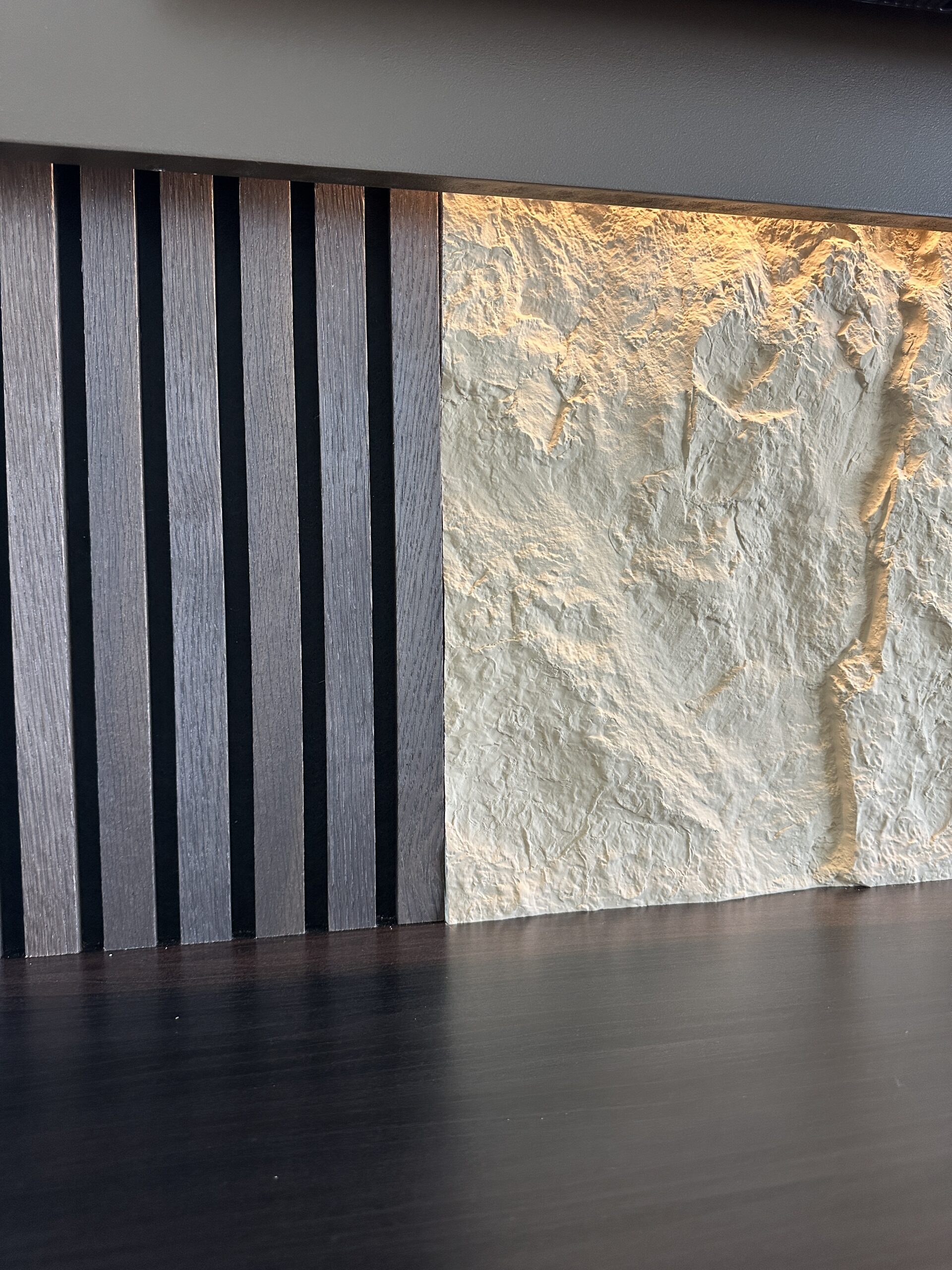 Close-up of dark vertical slats meeting light textured panels above the floating cabinet