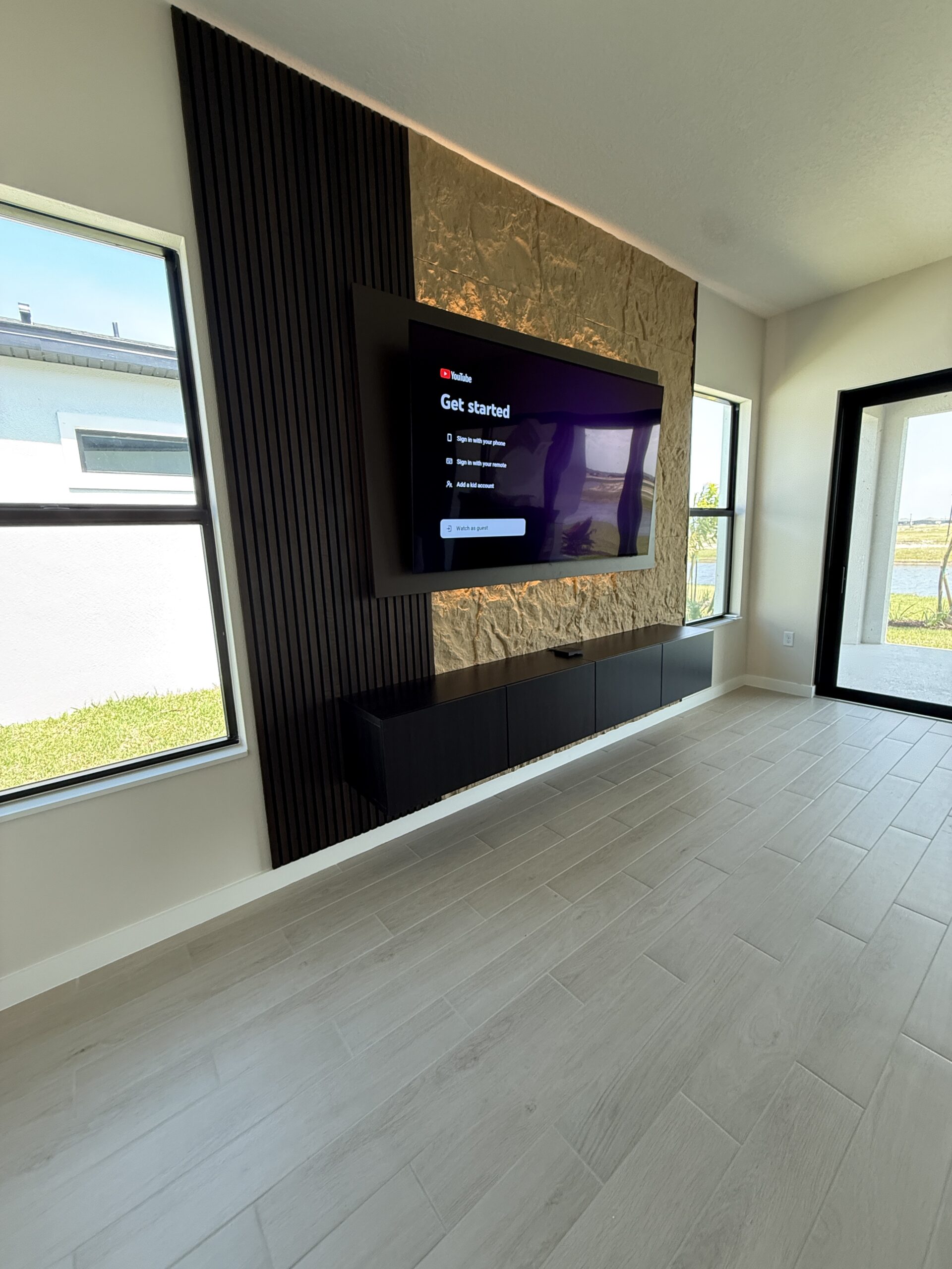 Wide room view of a finished TV wall with a dark floating media cabinet between two windows